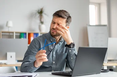 A man sitting at a computer and rubbing his dry eyes